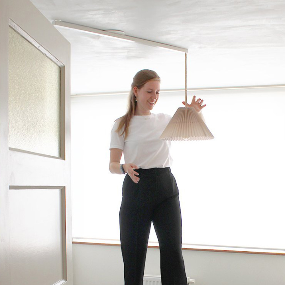 A woman hangs a pendant light on the Lightswing Single white